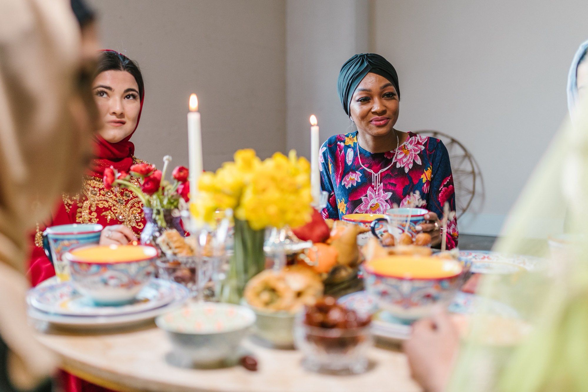 Women in hijab and head wraps sharing a candle-lit meal with dates.